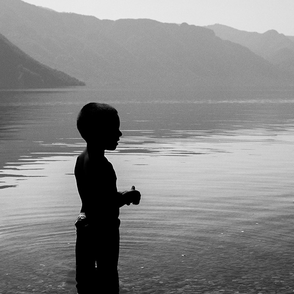 Una foto di silhouette di un bambino in piedi nell'acqua con le montagne sullo sfondo viene utilizzata come immagine di copertina del servizio fotografico di famiglia e lifestyle.