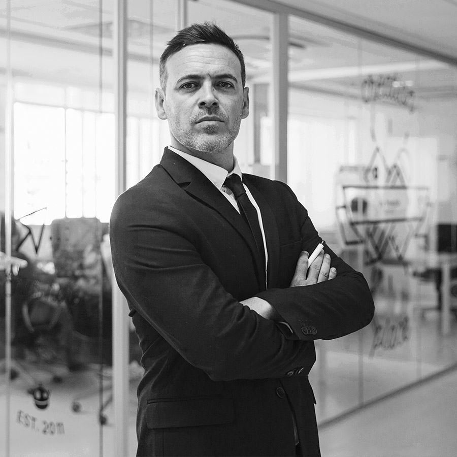 Portrait of a business man standing with hands tight wearing black suit with the office on a background.